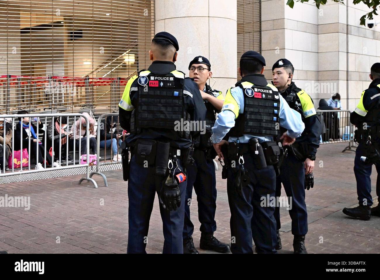 Police officers stand guard in front of people who had lined up all night  hoping to attend the trial in Hong Kong on December 15, 2025. Hong Kong  court has found Apple