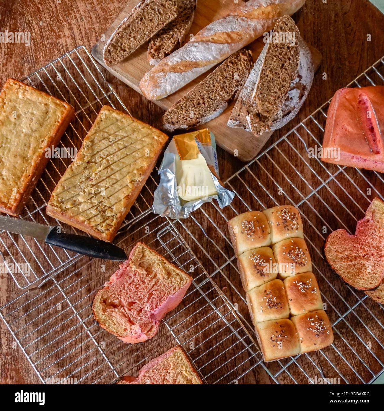 Assorted homemade bread with butter on cooling racks, rustic bakery food background Stock Photo
