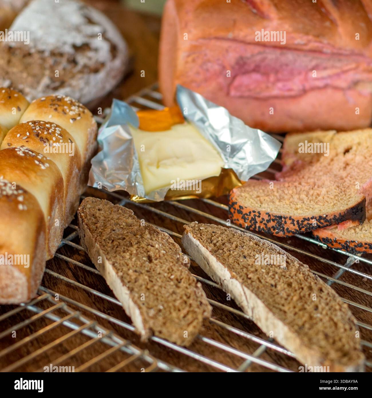 Assorted bread selection with butter on cooling rack, rustic bakery food background Stock Photo