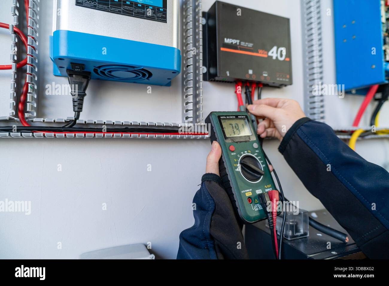 Hands using a multimeter to test electrical current on a solar charge controller Stock Photo