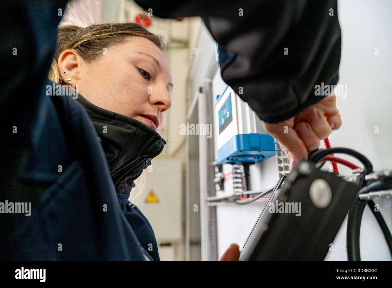 Woman engineer using tablet checking electrical panel connections with a colleague Stock Photo
