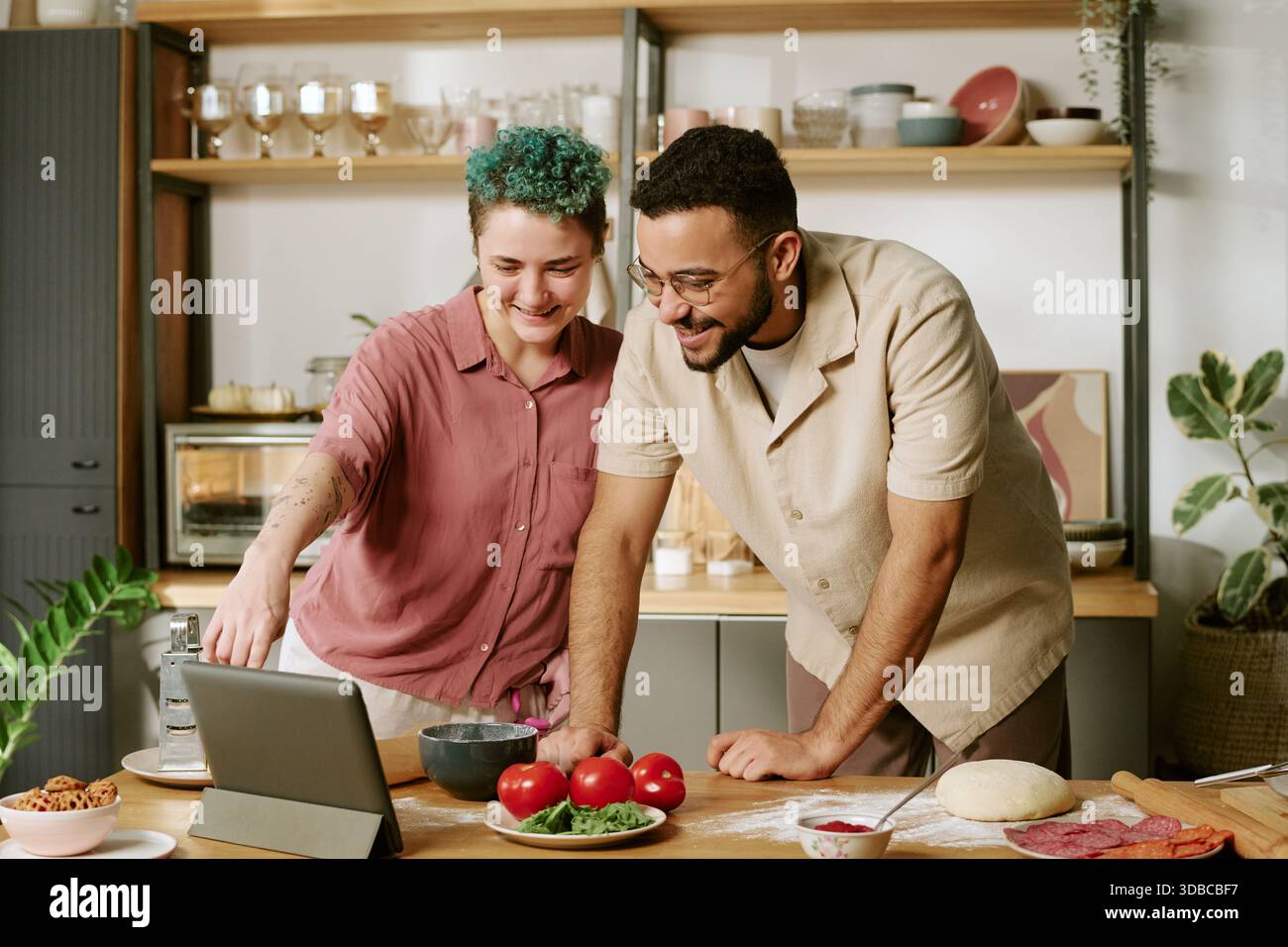 Young Woman and Young Man Cooking Together Using Tablet in Kitchen Stock Photo