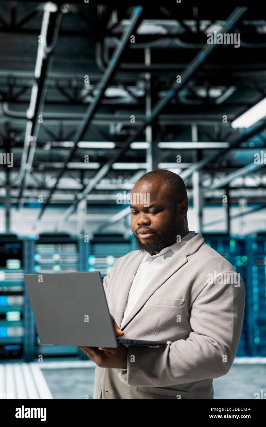 Server room IT specialist doing gear scans, fixing network issues affecting rigs performance. Data center engineer runs system diagnostic tests on notebook, tracking resource utilization Stock Photo