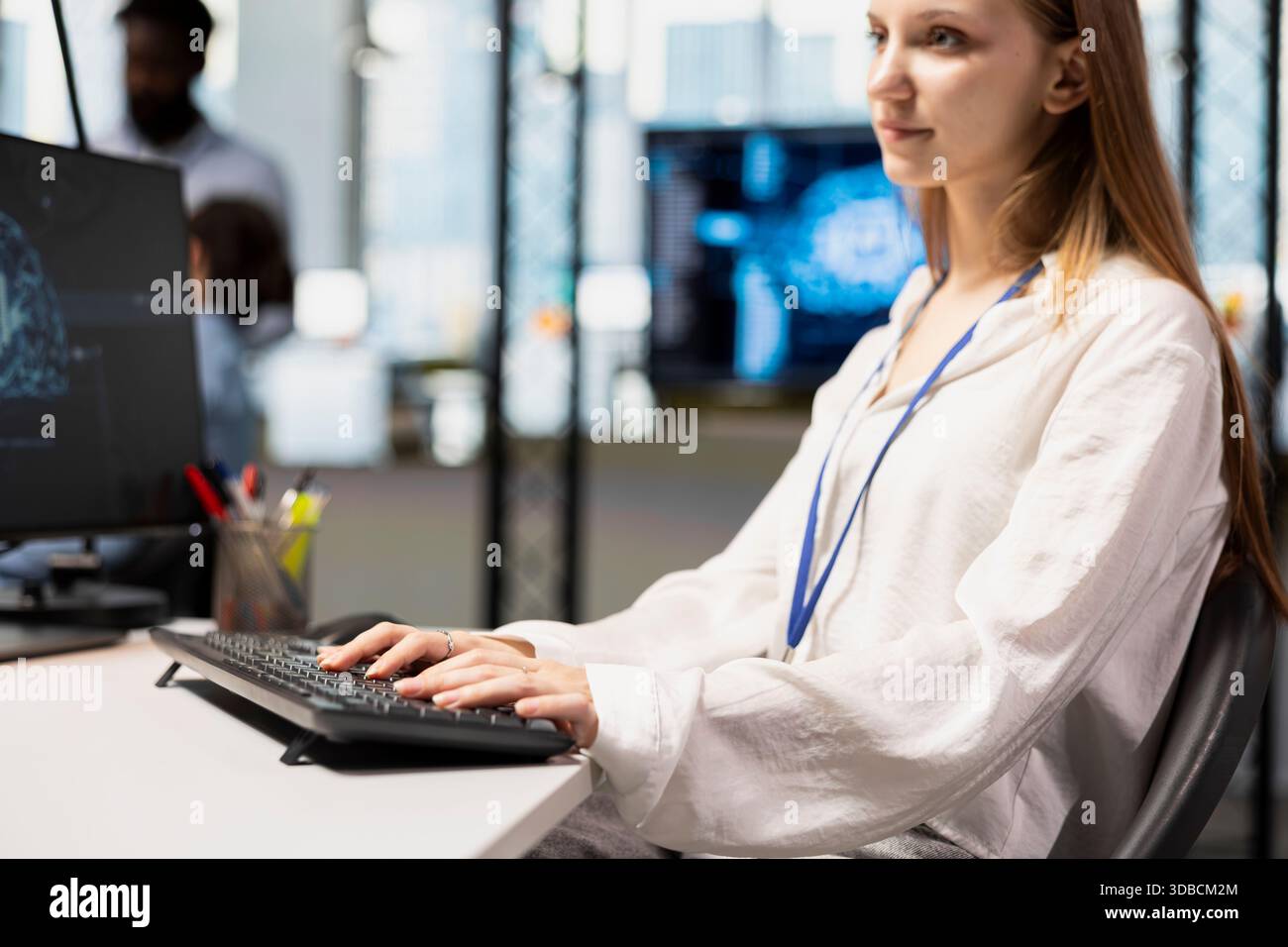 Jolly junior dev in office using AI on computer to streamline app development. Young female engineer at desk using PC to run debugging programs with machine learning technology Stock Photo
