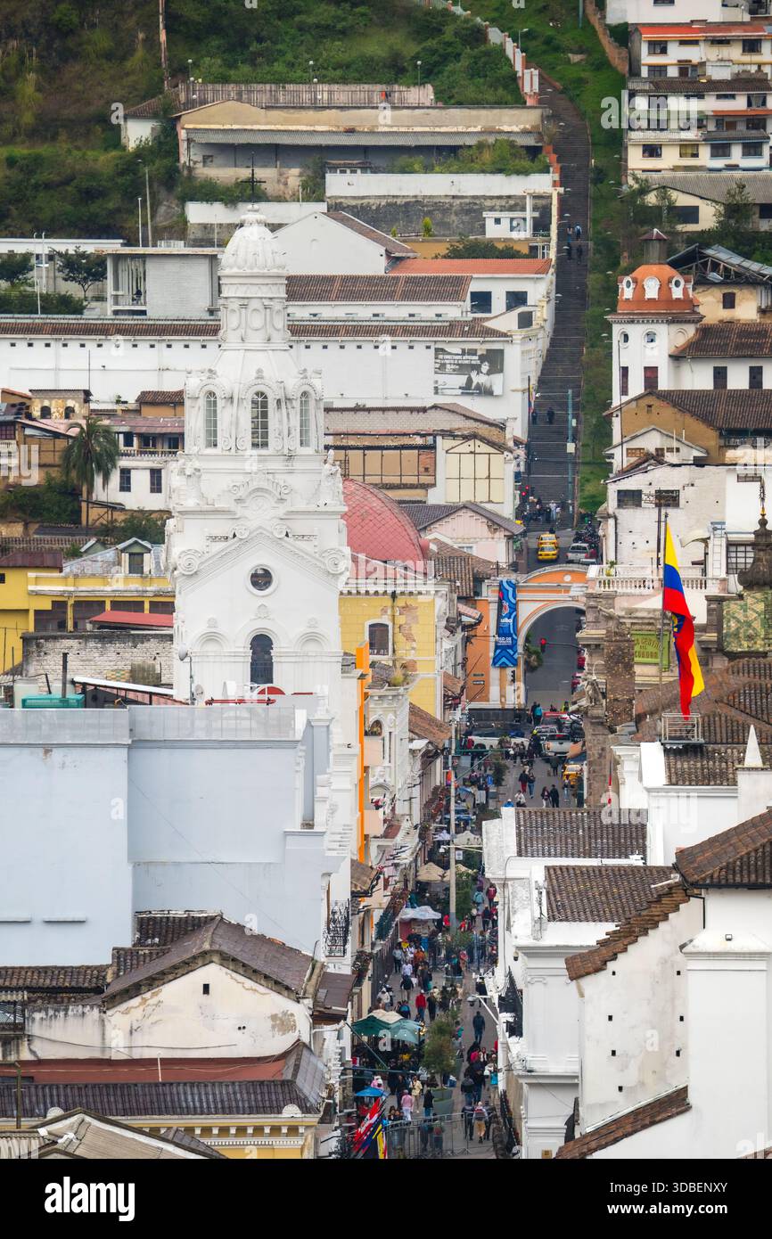 View of a bustling street lined with colonial architecture, a dominant white church steeple piercing the sky, and the vibrant Ecuadorian flag flutteri Stock Photo