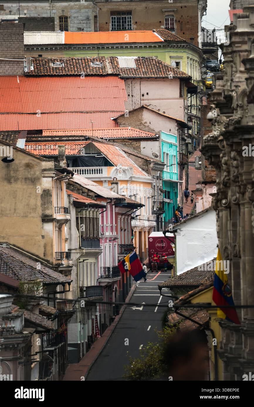 View of a steep city street adorned with colorful buildings and Ecuadorian flags fluttering gently, a ground-level perspective capturing the vibrant a Stock Photo
