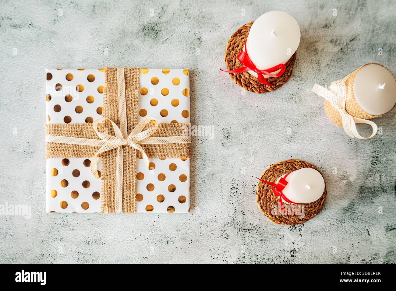 Holiday flat lay with white candles and a rustic gift wrapped in polka dot gold paper and burlap ribbon. Cozy and minimal festive setup Stock Photo