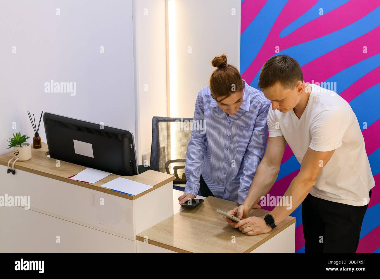 Man and woman at colorful wall desk verifying order via mobile Stock Photo