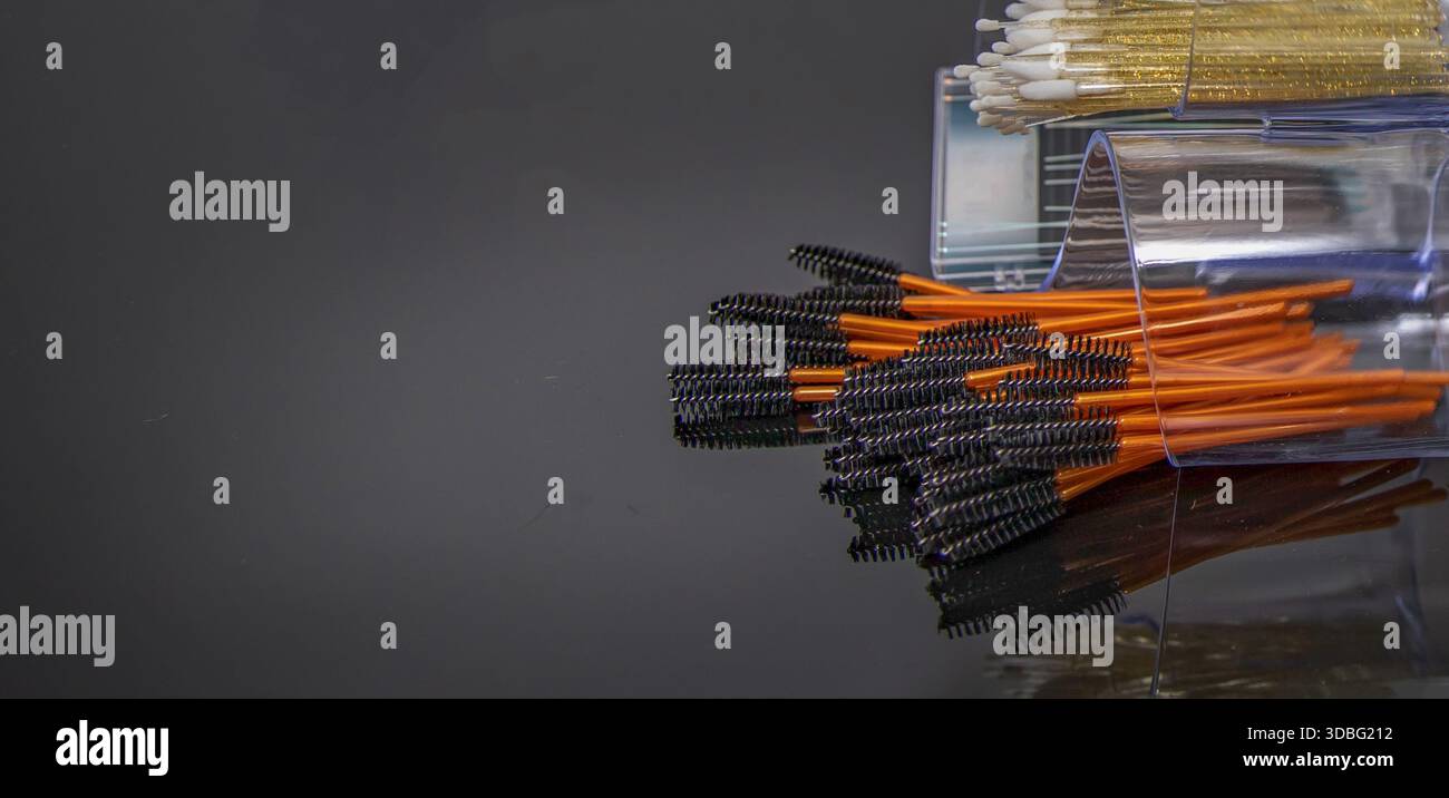 Disposable mascara brushes in transparent containers on reflective studio surface Stock Photo