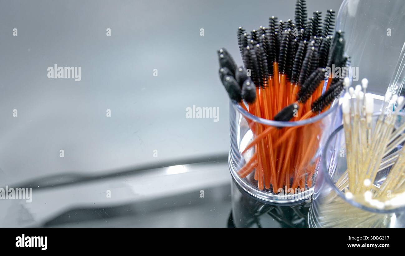 Disposable mascara brushes in transparent containers on reflective studio surface Stock Photo