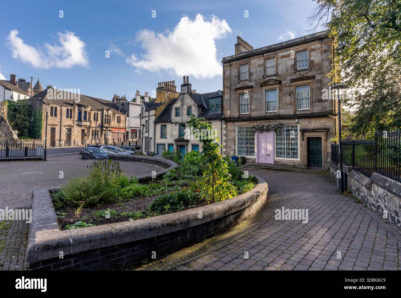 Quaint Scottish town centre scene in Dalry, Ayrshire, with stone buildings, curved brick path, and sunshine. Stock Photo