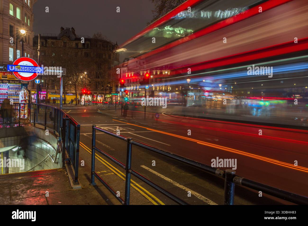 Red London bus driving down Trafalgar Square, London. Night scenes. Long exposure. Traffic scenes. Night scenes. Stock Photo