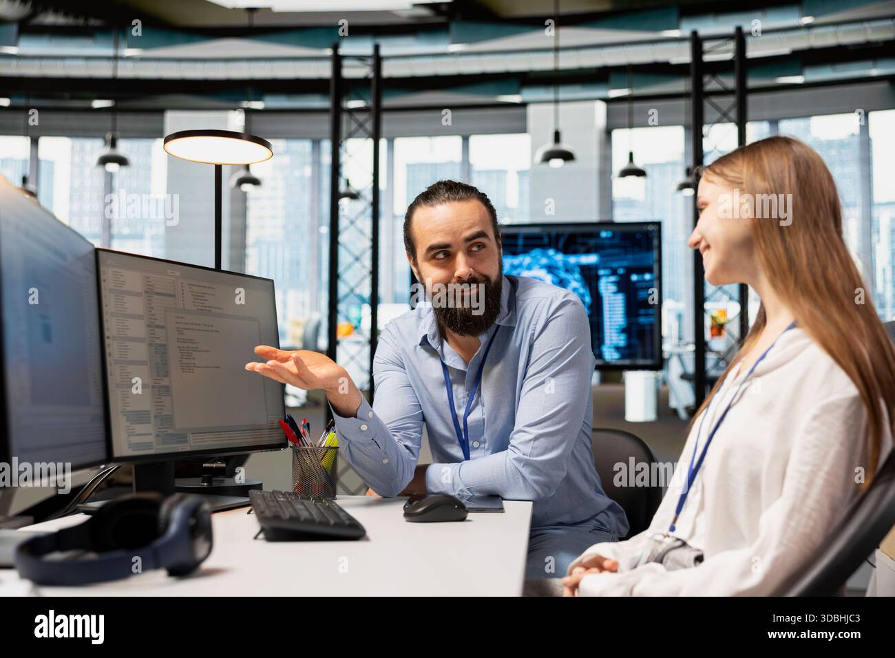 Happy IT professional teaching intern to use artificial intelligence. Smiling team leader programmer guiding junior dev through AI tool integration, mentoring her on using machine learning APIs Stock Photo