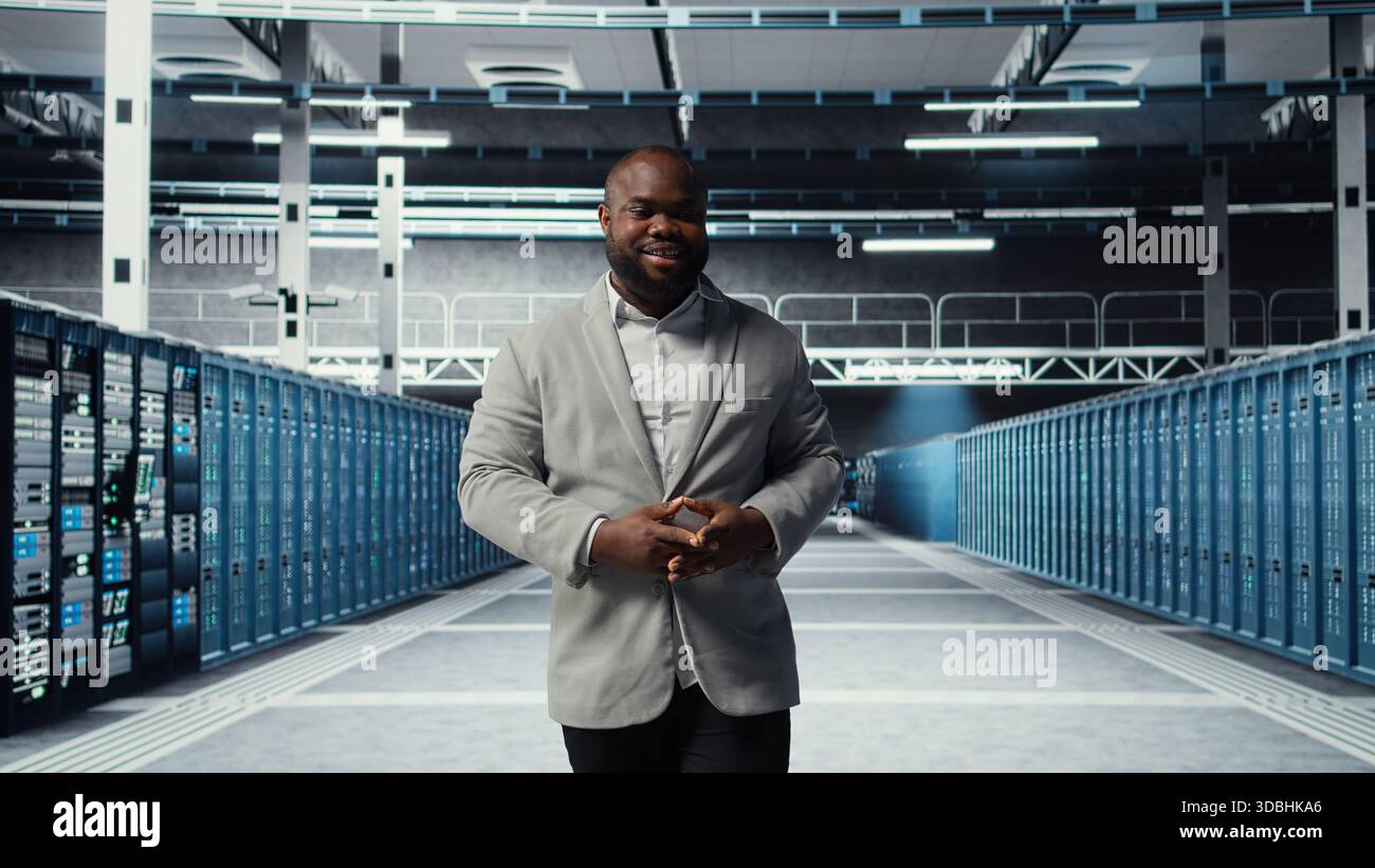 Cheerful admin walking in data center workplace, checking gear for system stability. Jolly IT professional overseeing server hub, configuring racks, optimizing performance, camera A Stock Photo