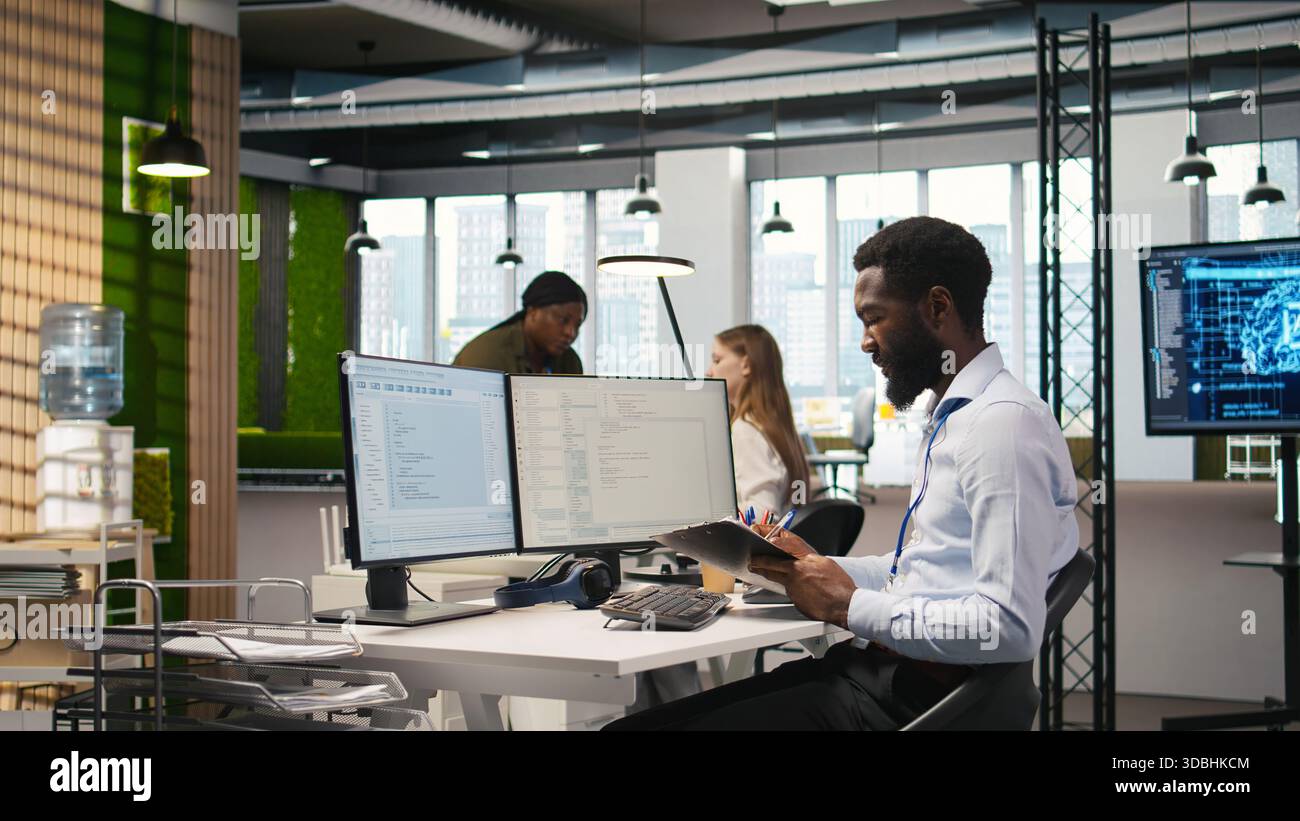 Admin in tech startup office using PC, compiling software patches to fix bugs, troubleshooting backend operations. IT expert running diagnostics, resolving system crashes via terminal, camera A Stock Photo