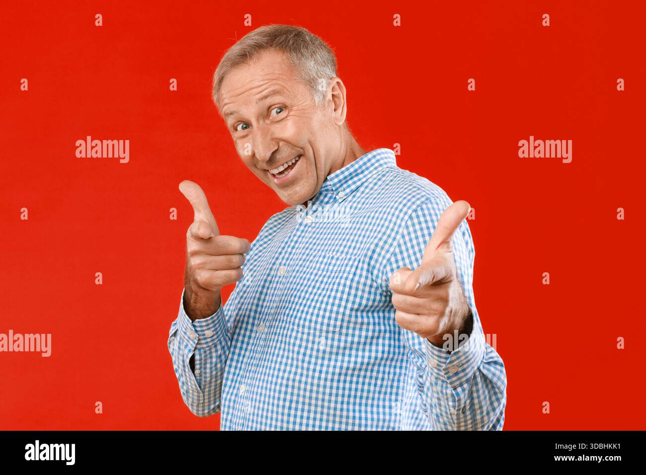 Older Man Smiling and Posing With Hand Gestures Against a Red Background Stock Photo