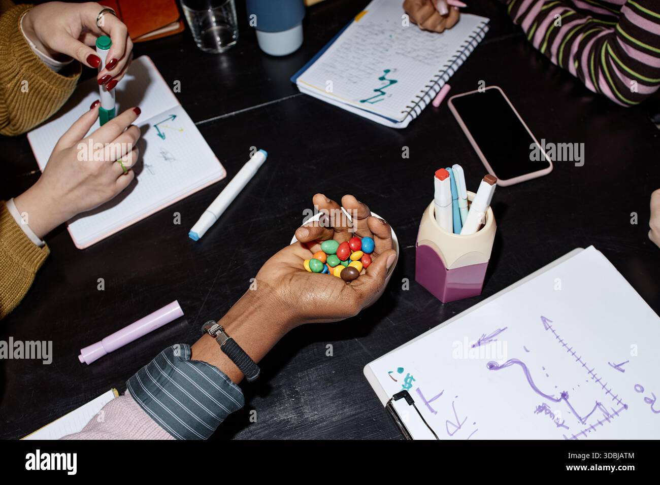 Multiethnic Young Adults Collaborating While Sharing Candy during Meeting Stock Photo