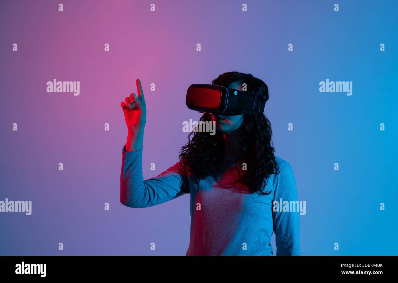 Woman using VR headset with neon blue red lighting while interacting with virtual interface in studio scene Stock Photo
