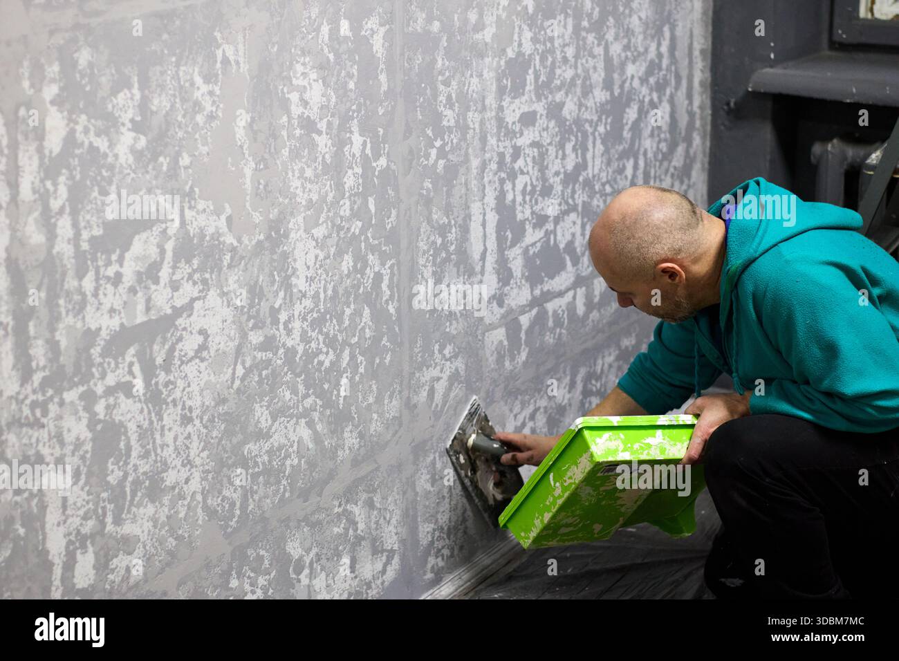 This image captures a construction worker meticulously applying decorative plaster to a wall. The worker is using a trowel to create a textured, moder Stock Photo