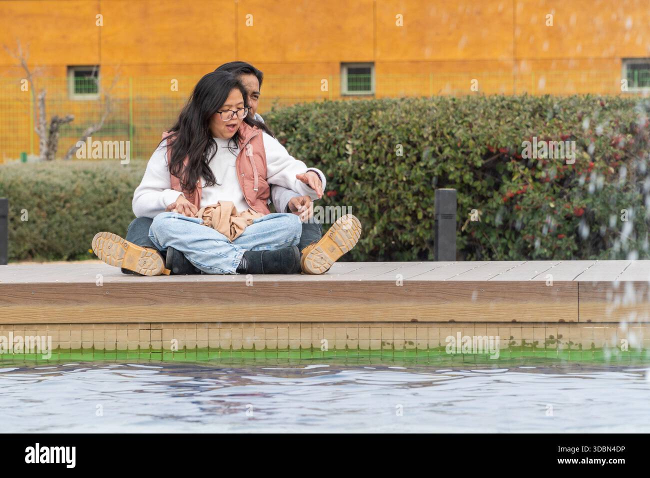 Multiehnic couple sitting together by fountain enjoying playful moment outdoors Stock Photo