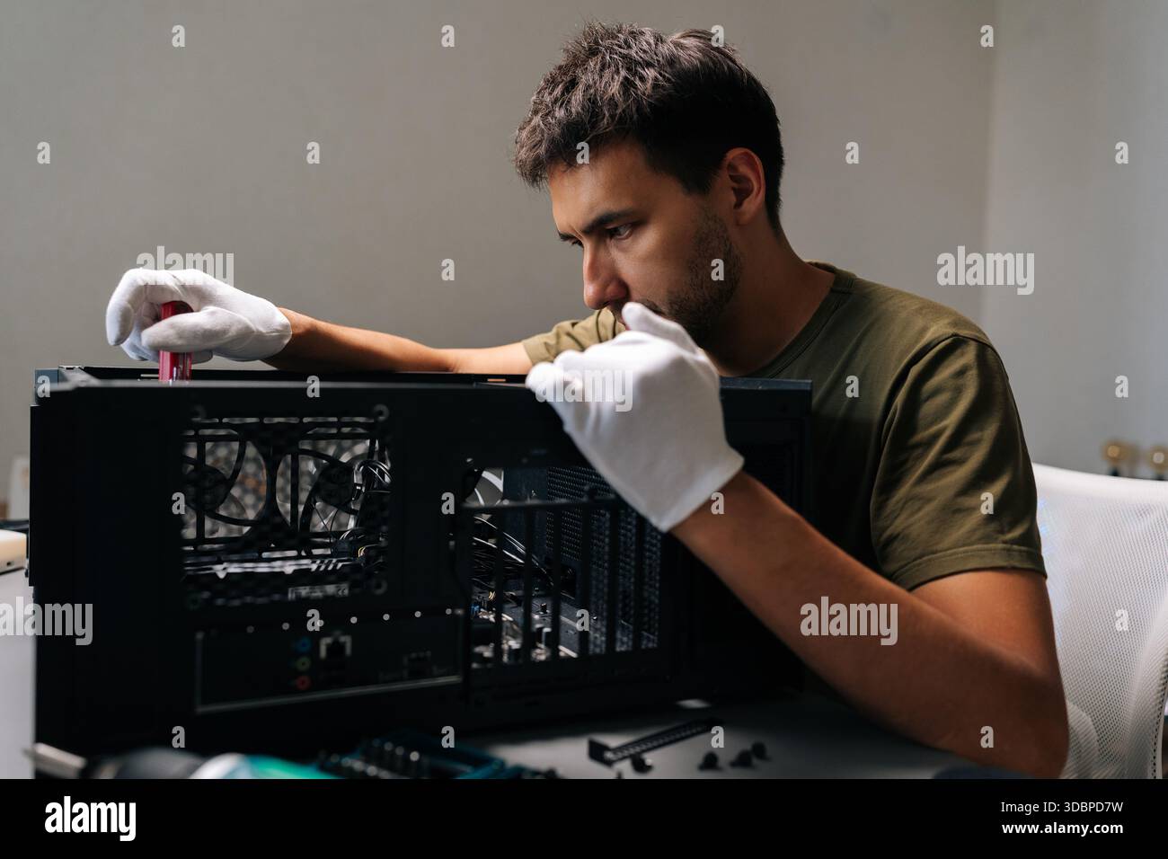 Focused computer technician in protective white gloves carefully installing internal hardware components inside open desktop computer case Stock Photo