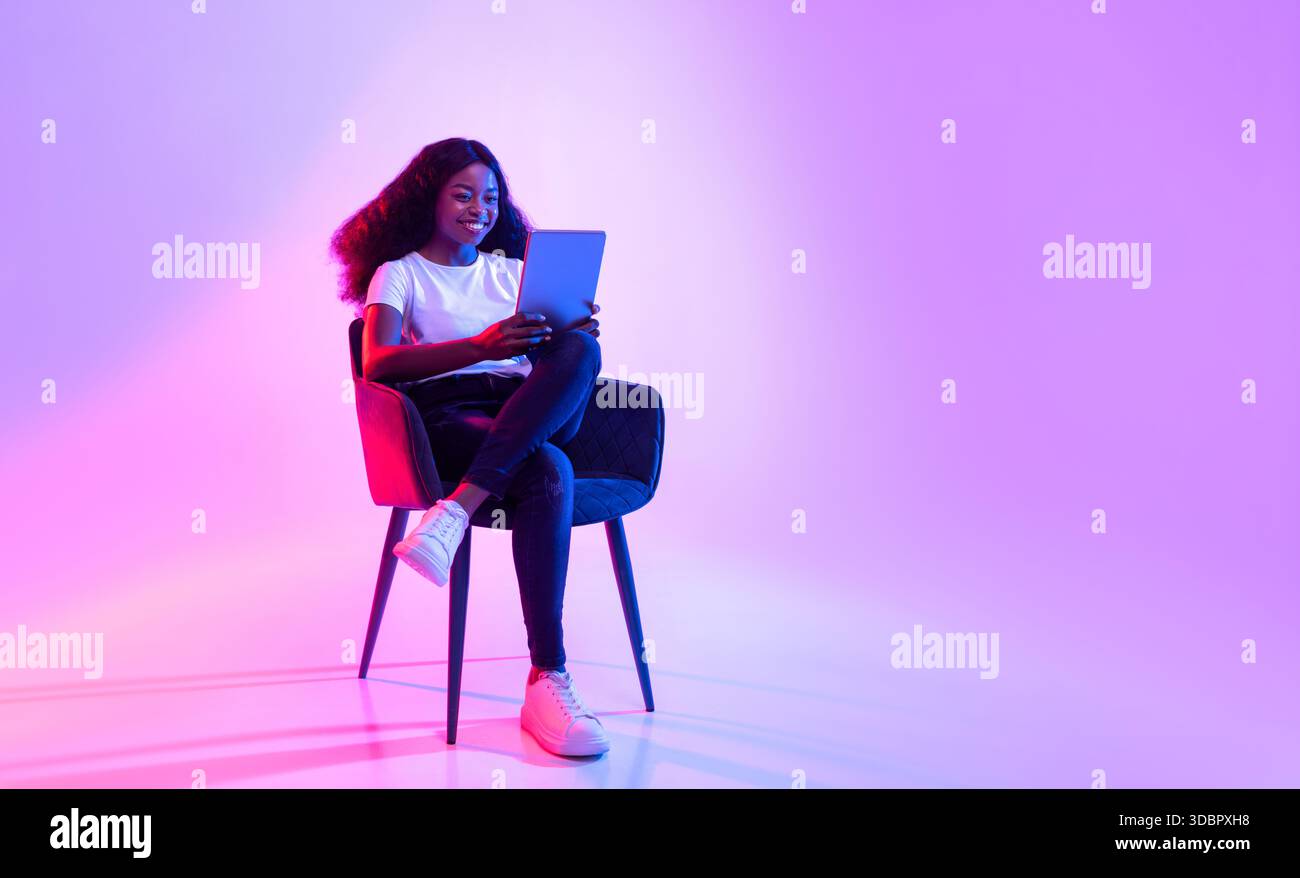 Cheerful Young Black Lady Enjoying Online Study in Neon Light Environment Stock Photo