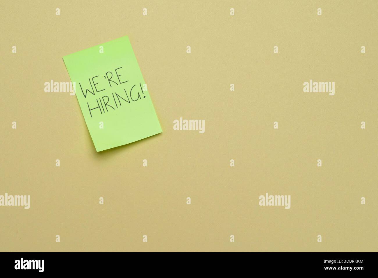 A green sticky note with the handwritten message WE'RE HIRING! on a plain background. Job openings, recruitment, talent acquisition, and employment Stock Photo