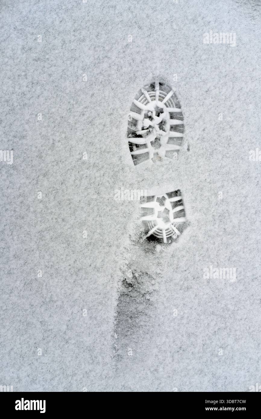 Single deep boot sole tread imprint in fine fresh snow, vertical top-down view, white granular surface, dark rubber pattern visible, overcast daylight Stock Photo