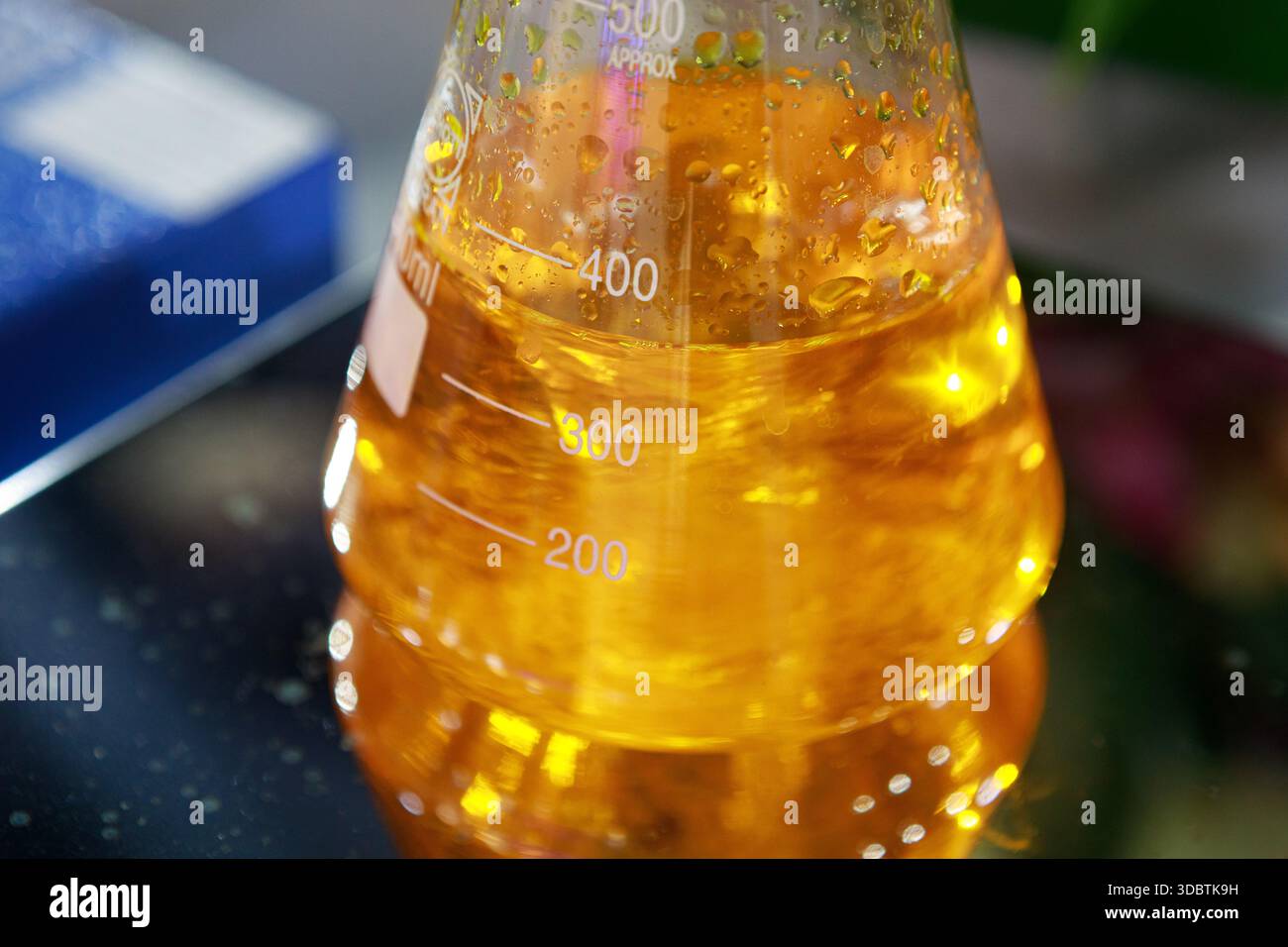 A close-up of a glass Erlenmeyer flask filled with a vibrant orange ...
