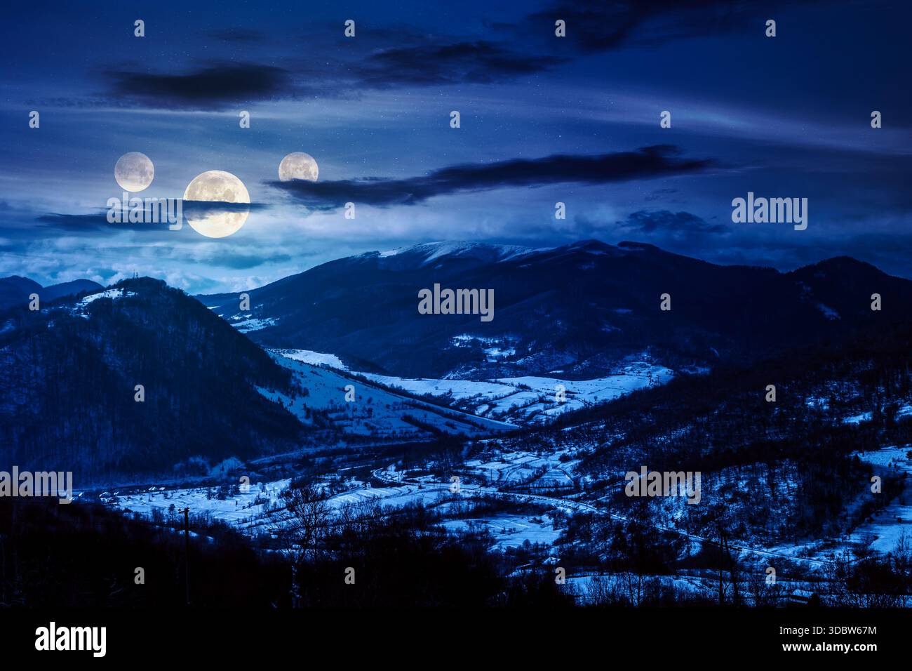 mountainous rural landscape in winter at night. snow covered fields on hills in full moon light. village in the valley. landscape with clouds on sky. Stock Photo