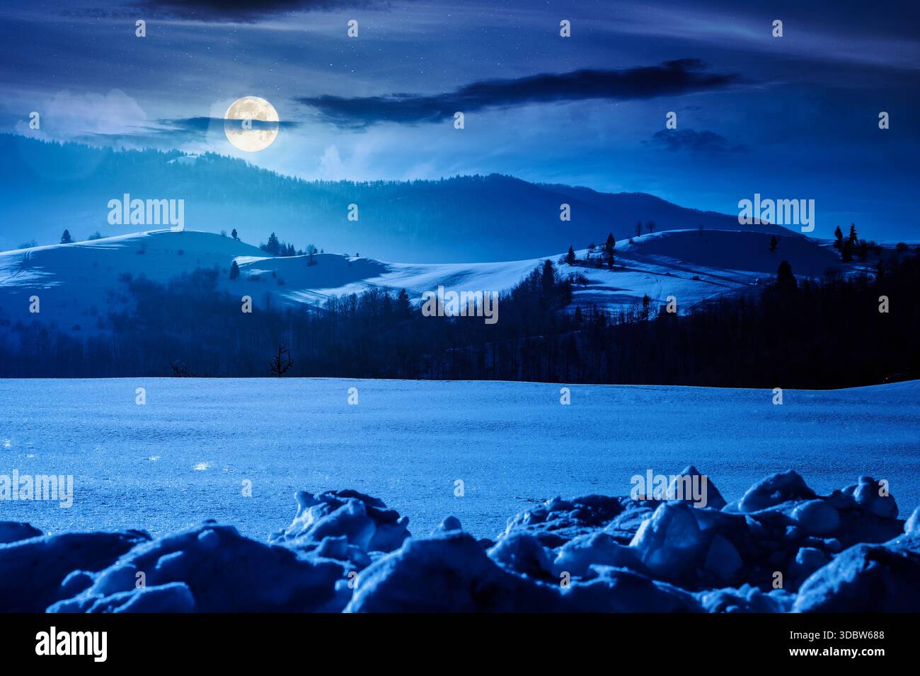 beautiful winter landscape with snow covered rolling hills under dark sky at night. majestic mountains in full moon light. frosty countryside scenery. Stock Photo