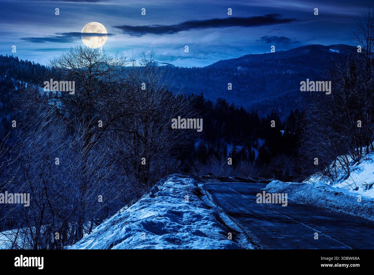 country road winding through winter landscape under dark sky at night. mountains in full moon light. travel background with pass and snow covered slop Stock Photo