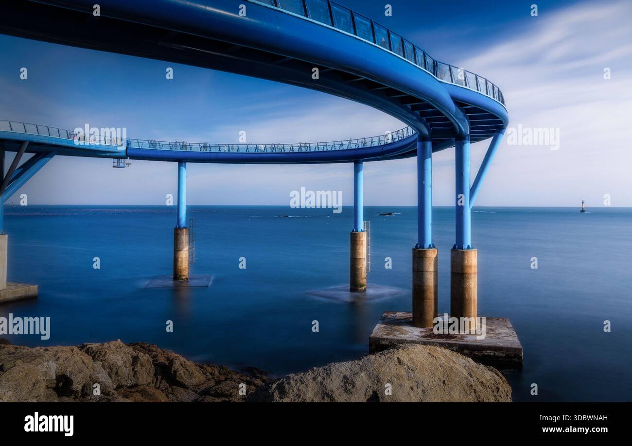 View of the graceful, ultramarine curved skywalk arches over the serene, silky ocean, a modern marvel against the rocky coast, Busan, Busan, South Kor Stock Photo