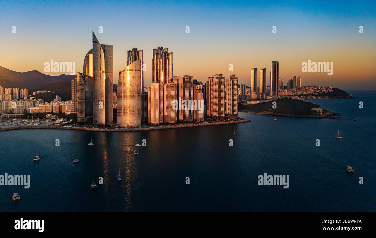 Aerial view of sun-kissed skyscrapers reflect golden light over Haeundae Beach, contrasting with the deep blue sea, Busan, Busan, South Korea. Stock Photo