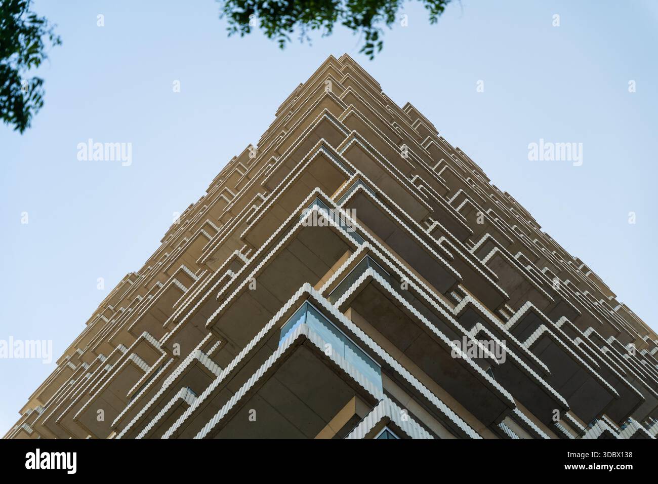 View of angular balconies jutting from a modern high-rise, reaching toward the light blue sky, a stark contrast against the building's sharp lines, Vi Stock Photo