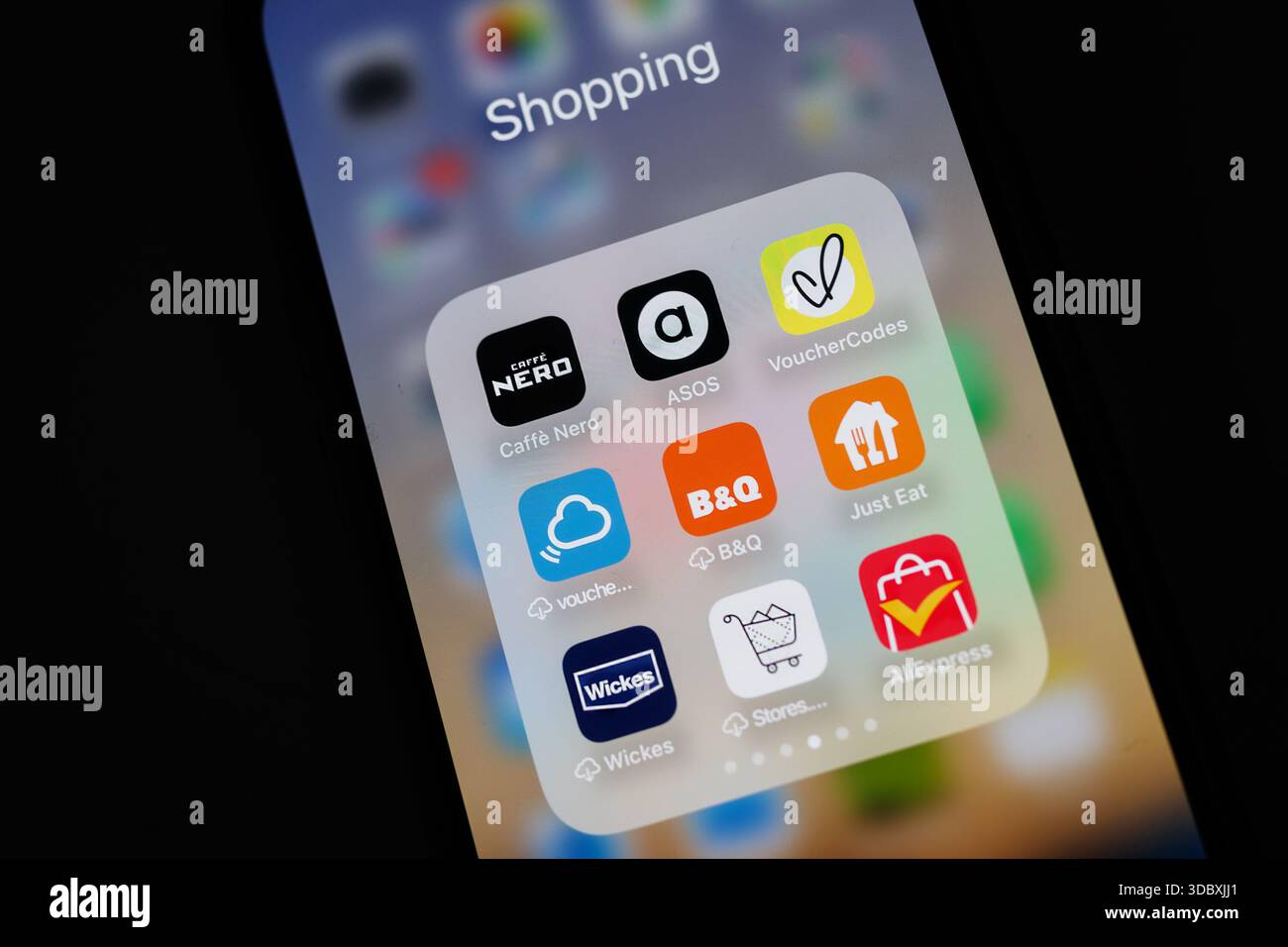 Close-up of a iPhone smartphone screen showing various shopping and discount apps organized in a folder labeled Shopping Aliexpress B&Q wickes Stock Photo