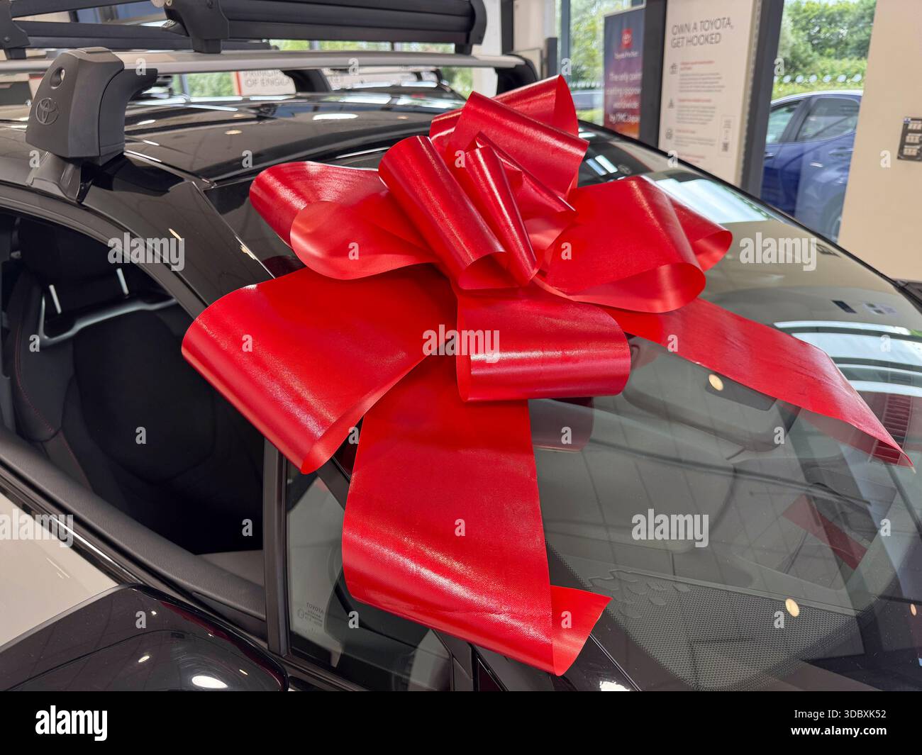 WIRRAL, CHESHIRE, ENGLAND - JUNE 27, 2025: A close up shows a red bow attached to the windscreen of a brand new car in a showroom in England - Smartphone Captured Stock Image