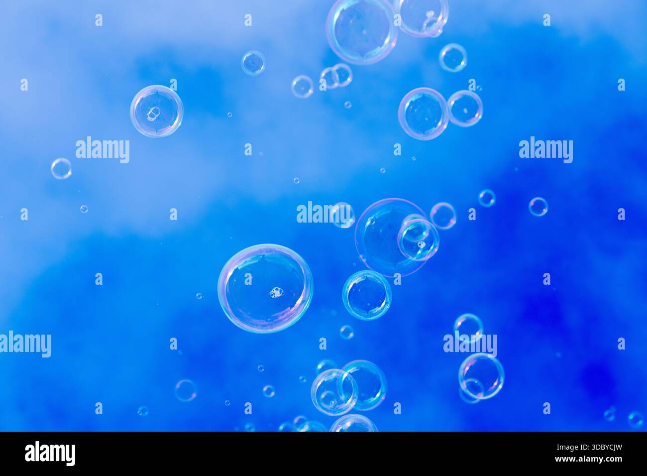 Small soap bubbles float upward against a bright blue sky with soft cloud patterns on a clear winter day. Stock Photo