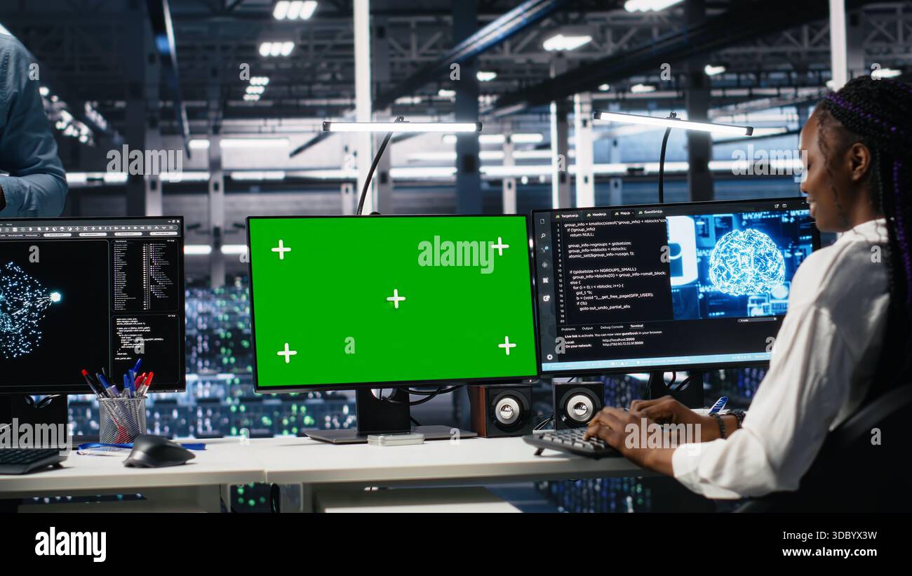 Female programmer talking with manager in data center, reviews AI diagnostics on green screen PC. IT expert and supervisor optimizes artificial intelligence systems using mockup computer, camera A Stock Photo