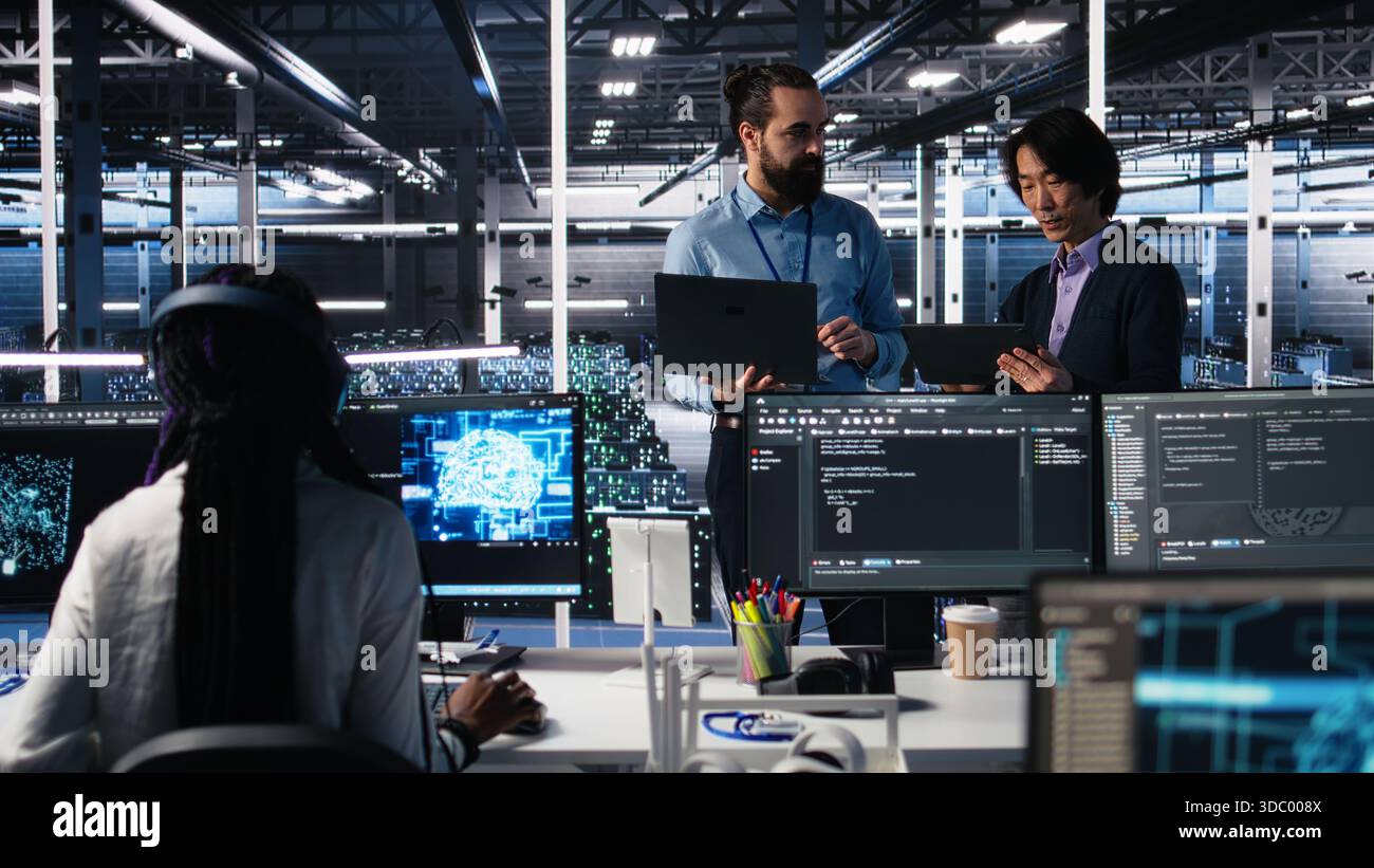 Data center manager supervising work done by programmers working on neural network software. Server hub supervisor overseeing IT staff members implementing deep learning tech, camera A Stock Photo