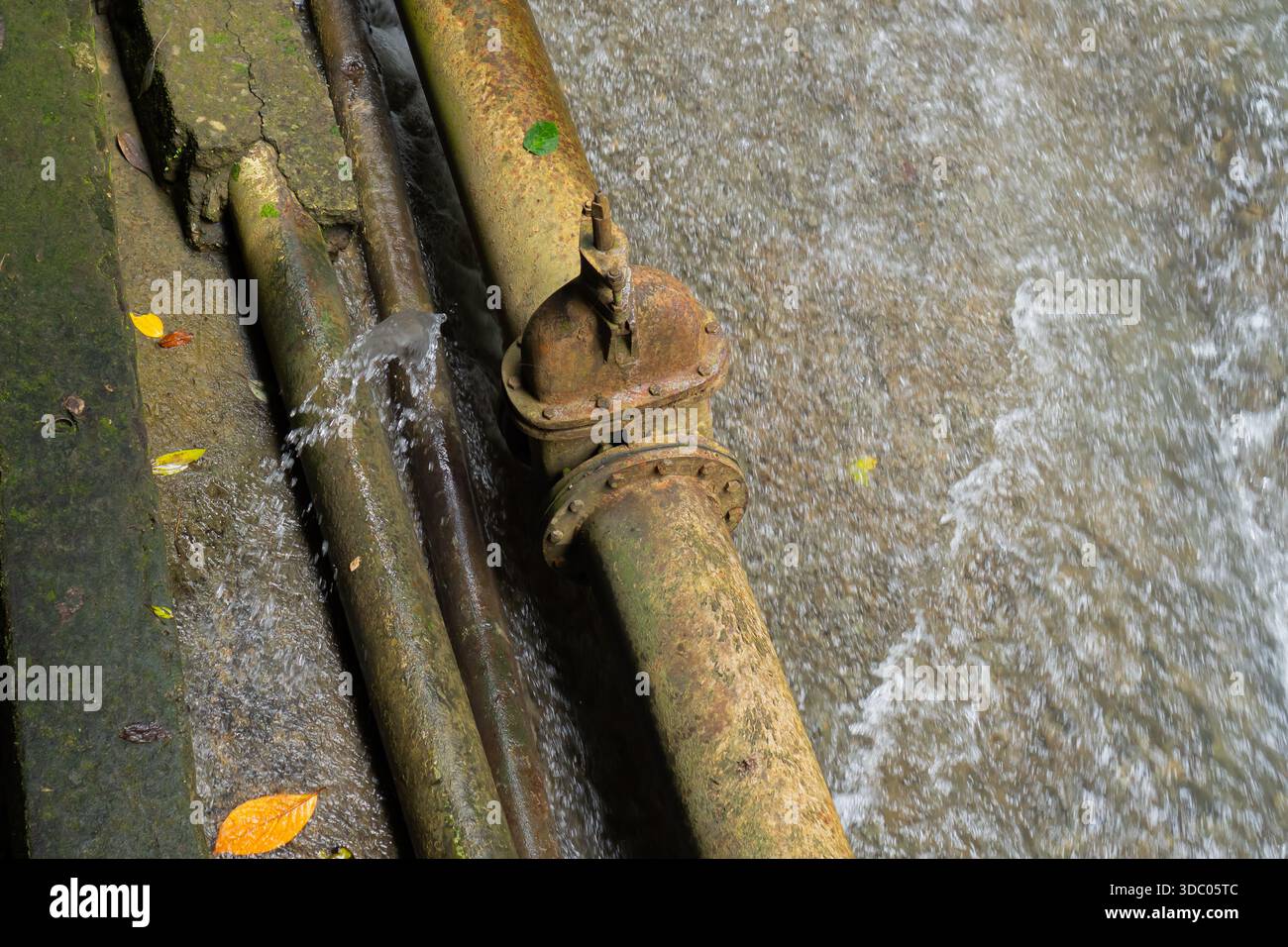 Close Up Of Old Rusty Water Pipes Partially Submerged In Flowing Water With Green Moss On Concrete Stock Photo