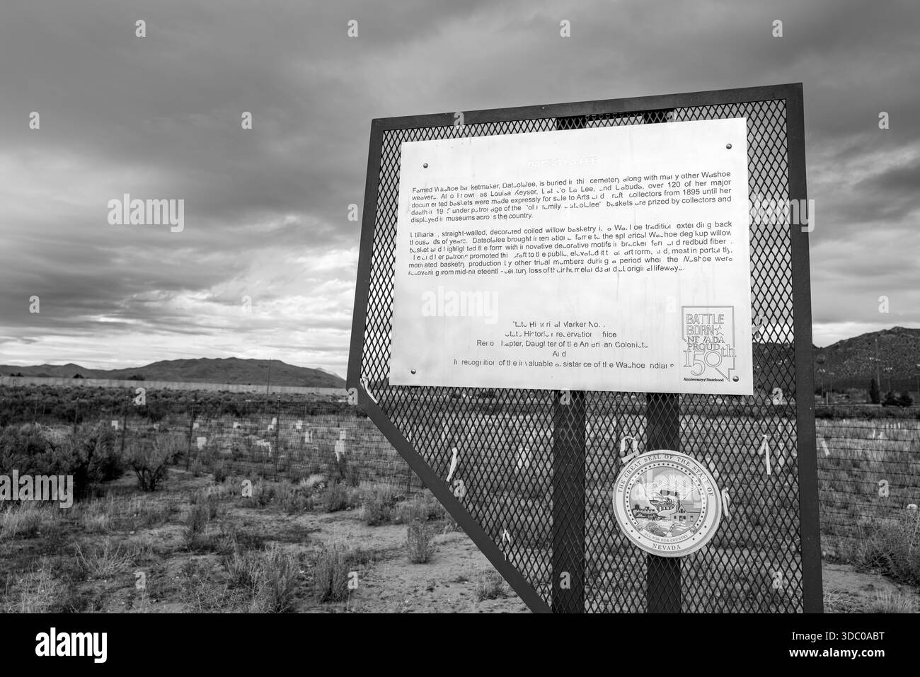 A black and white close-up of the Nevada 150th anniversary information sign at the Stewart Indian School Cemetery, grave markers and hills. Stock Photo