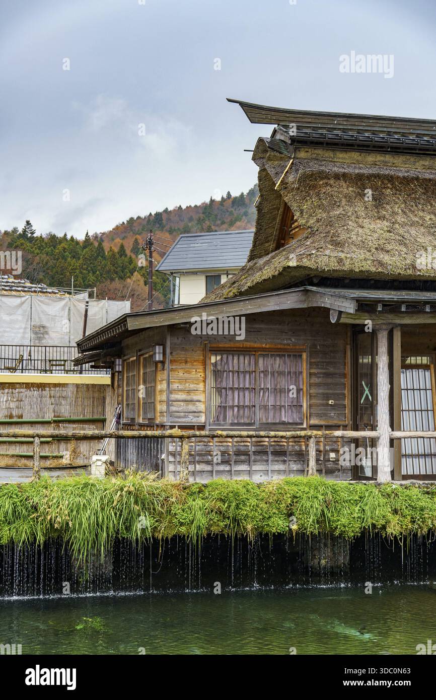 Traditional wooden house with thatched roof next to a watercourse in ...