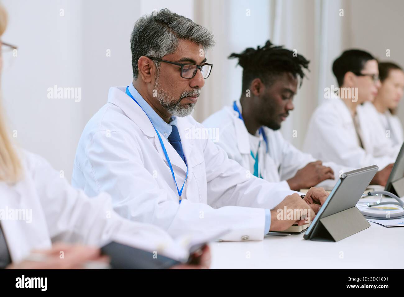 Middle Aged Man Collaborating with Diverse Medical Team Using Tablets Stock Photo
