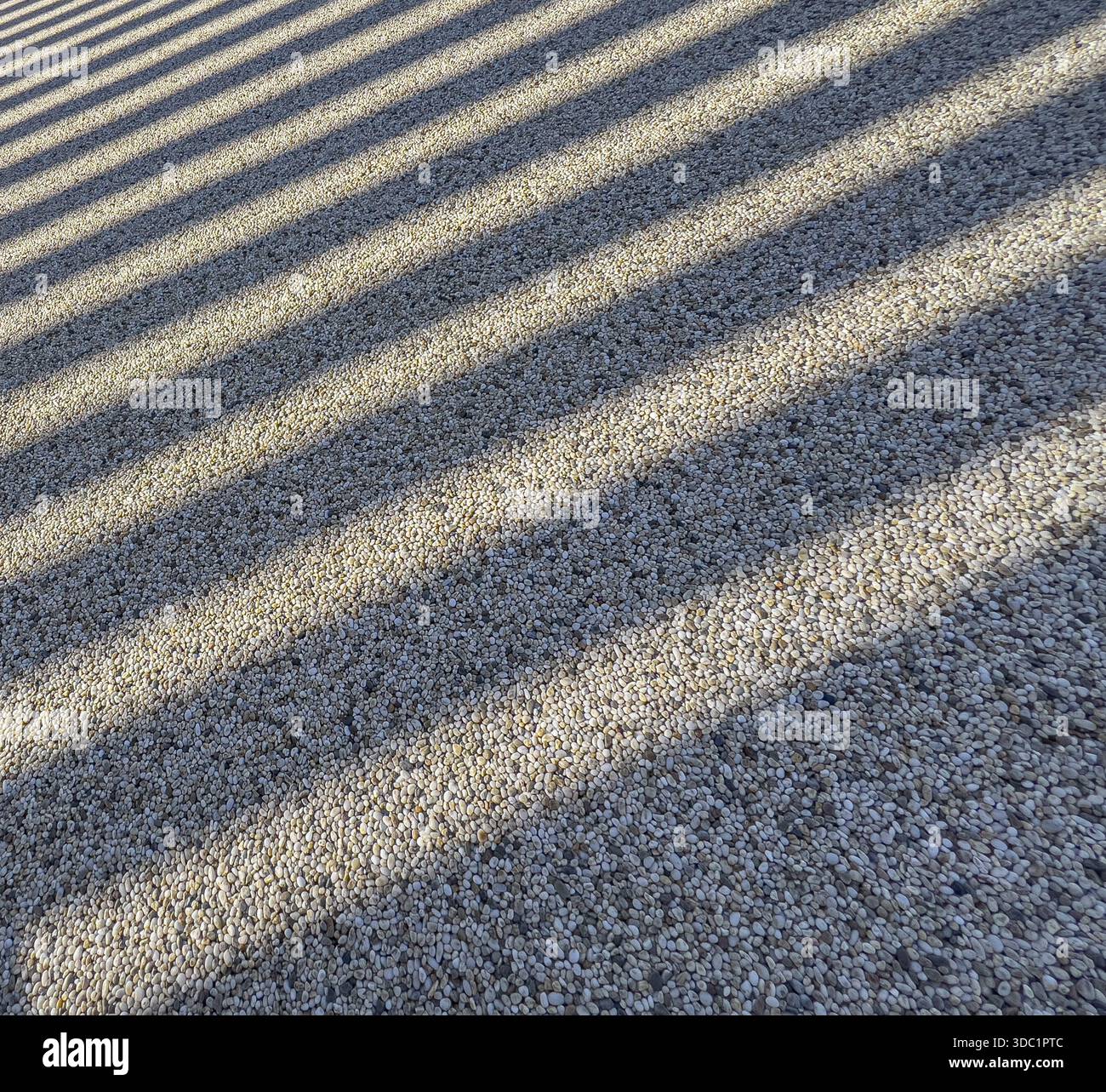 Geometric shadows casting parallel lines across a textured pebble surface Stock Photo