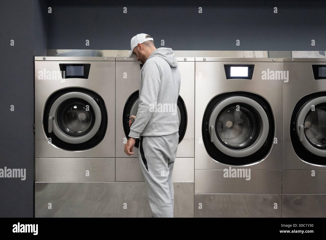 Man Using Self-Service Washing Machine in Modern Laundromat Stock Photo