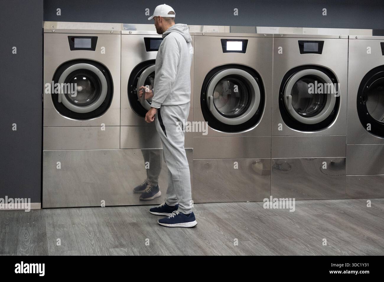 Man Using Self-Service Washing Machine in Modern Laundromat Stock Photo