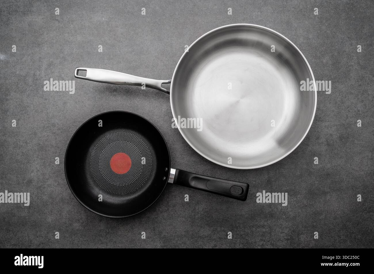 Top view of professional stainless steel and black non-stick frying pans on a dark grey stone background. Kitchenware and cookware concept. Stock Photo