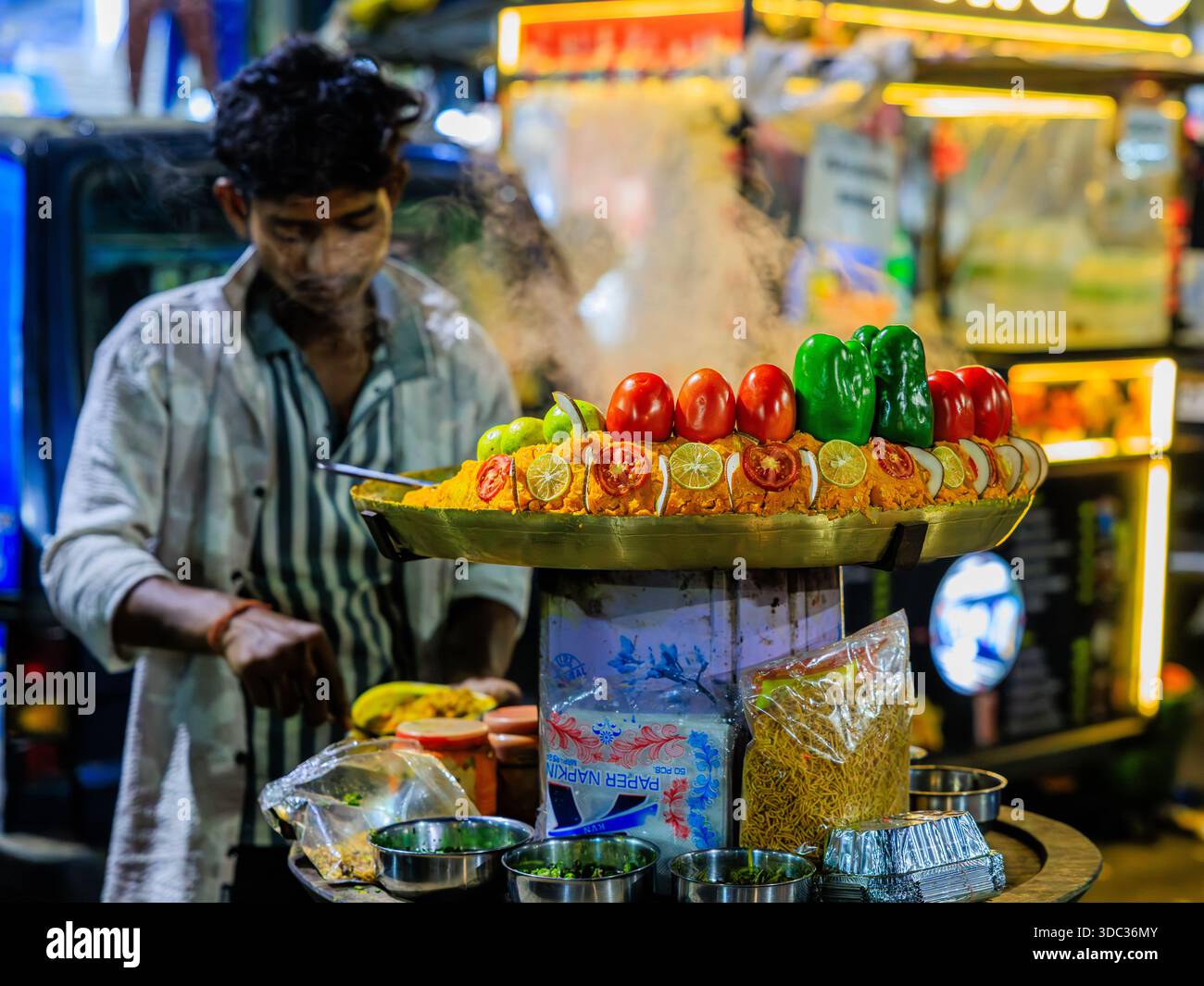 a colourful roadside streetfood stall in kolkata vendor is preparing food behind a steaming hot pan of rice decorated with whole tomatoes and peppers Stock Photo