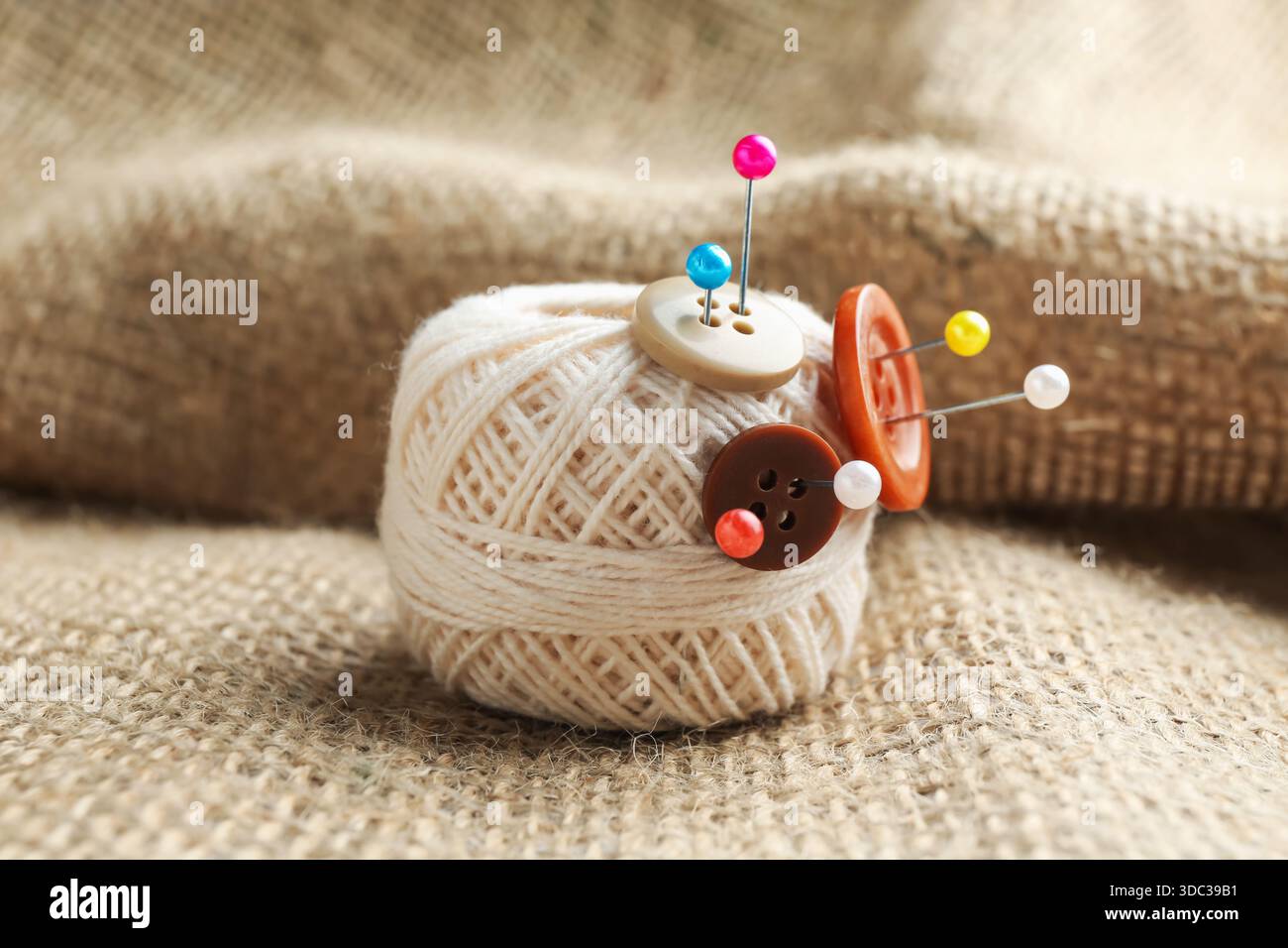 White yarn with pins and buttons on burlap cloth, closeup Stock Photo